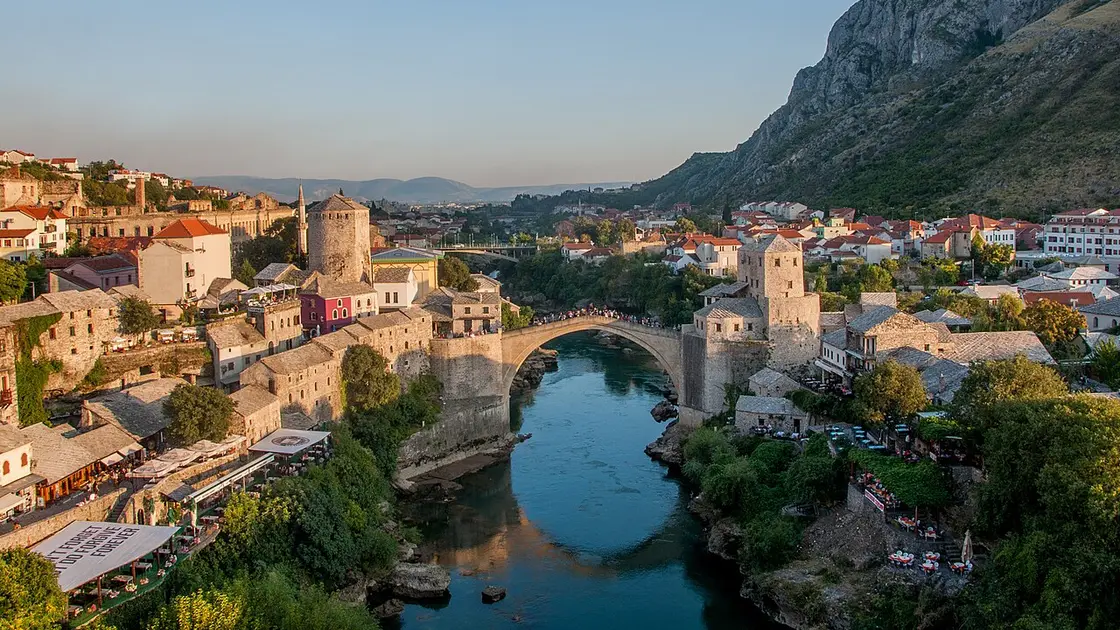 Golden evening view down the Neretva to the Old Bridge of Mostar, the bazaar and stone towers on both banks with the mountain beyond