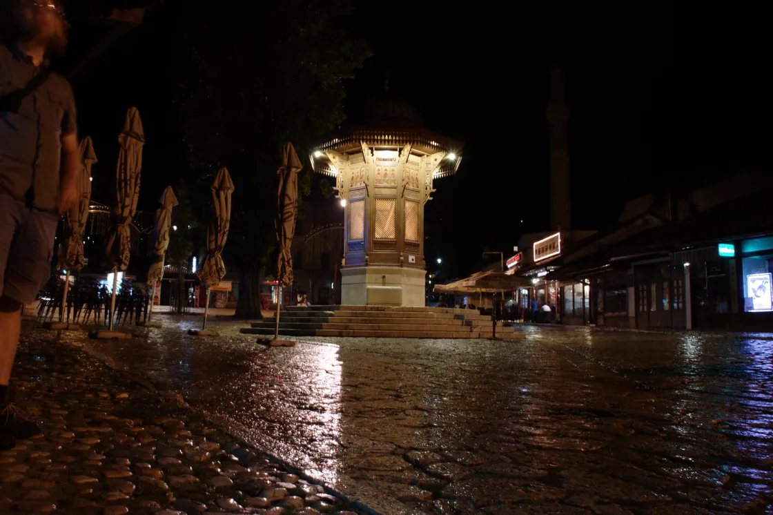 Baščaršija in the evening, low-rise Ottoman shopfronts and lit lanterns along the old bazaar street