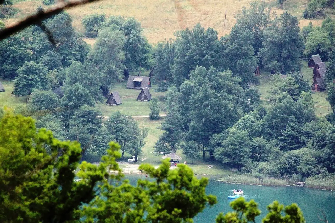 Boračko Lake under forested Prenj slopes with a still green surface
