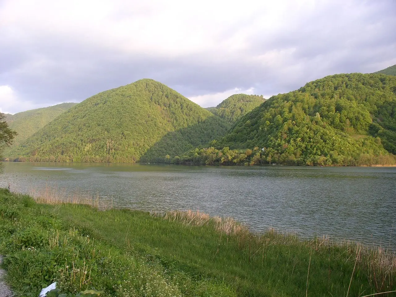 Wide green expanse of Veliko Plivsko Lake near Jajce under soft summer cloud