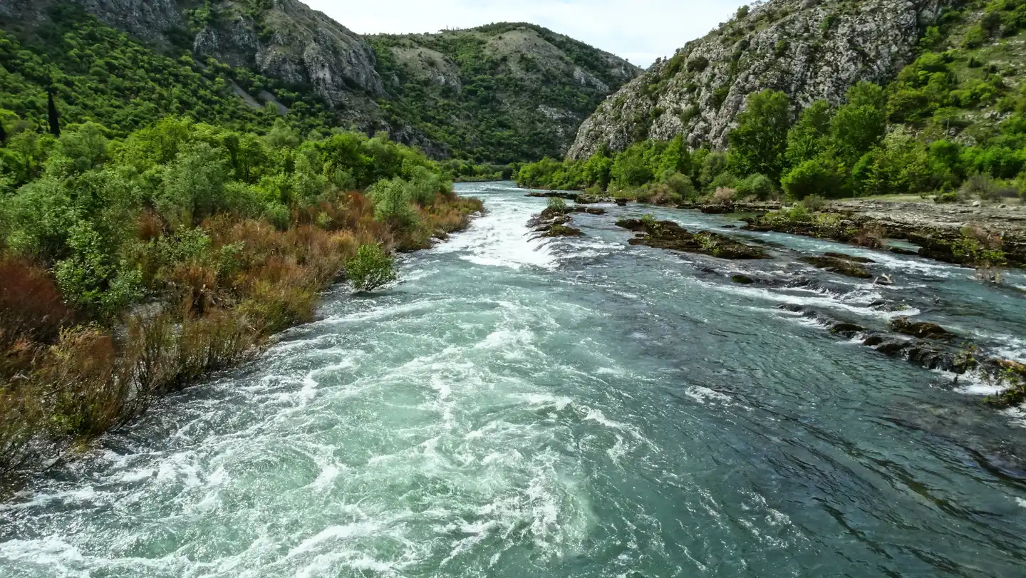 The turquoise Neretva river rushing through a green limestone gorge in Herzegovina under spring foliage