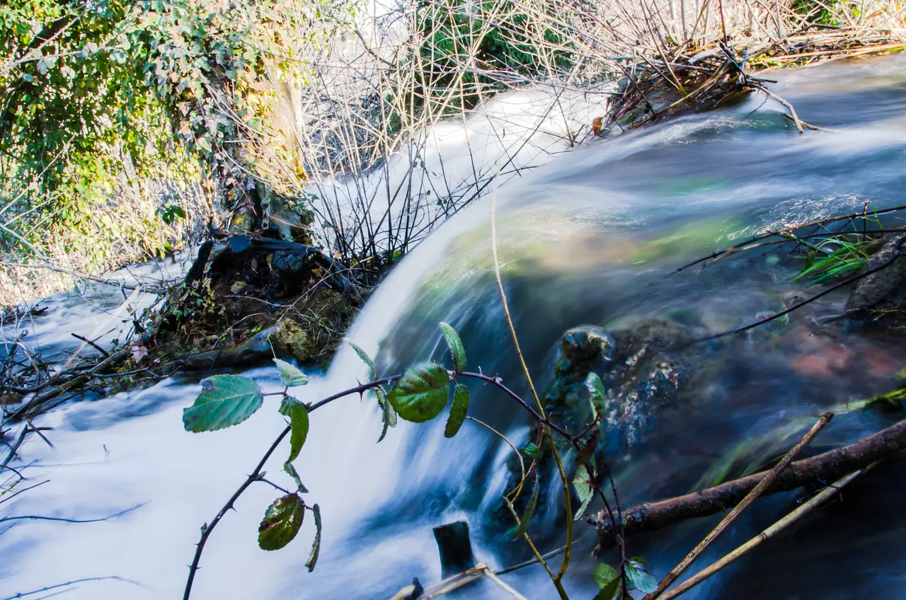The wide Kravice waterfalls running strongly over a green travertine ledge into a turquoise pool in spring