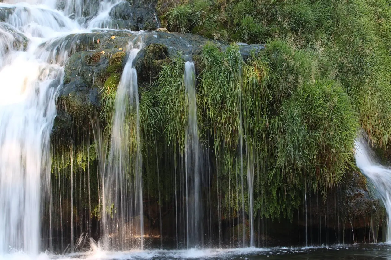 The wide, low water slide of Koćuša waterfall spreading across the Trebižat river over green tufa