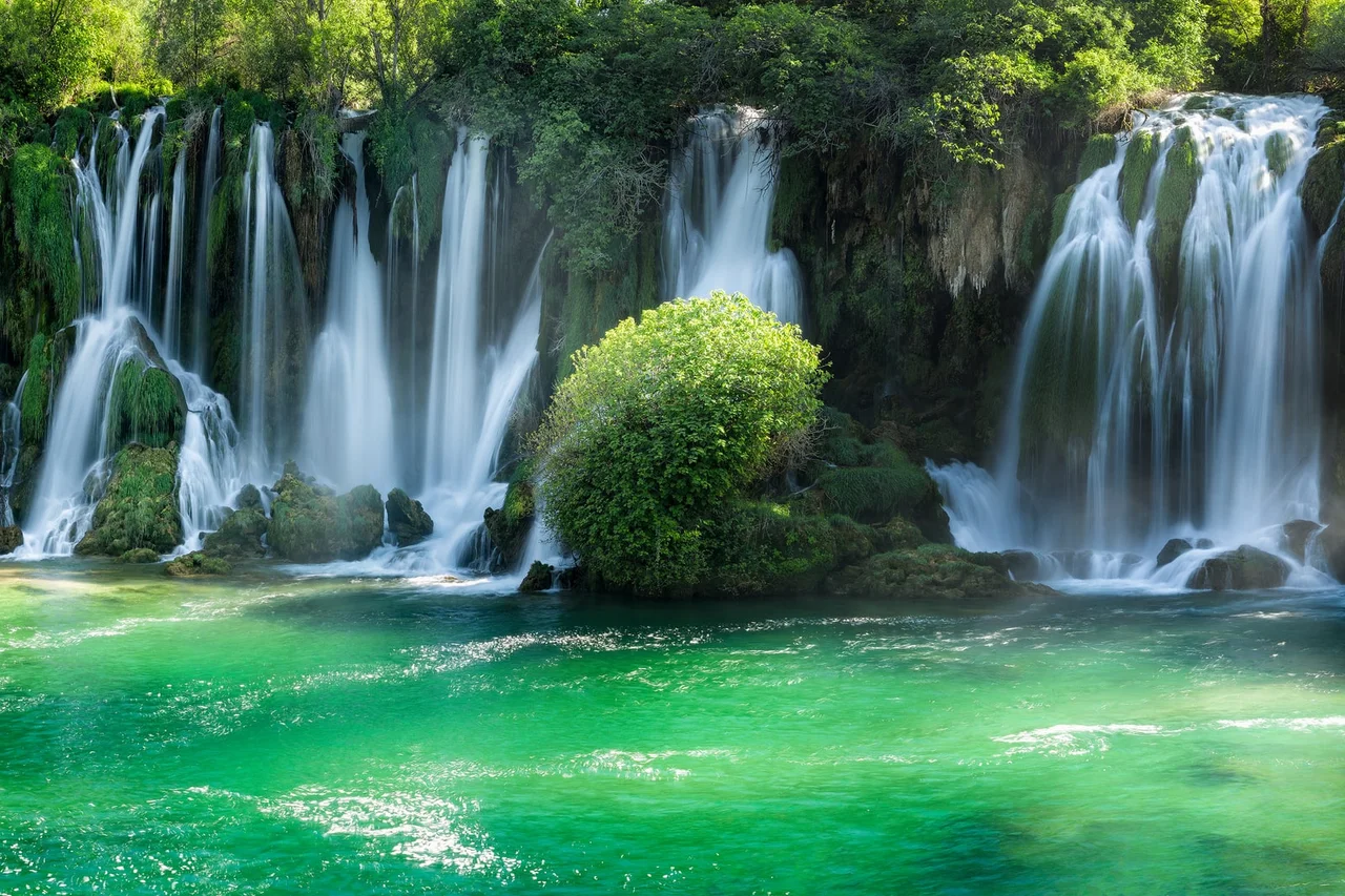 The Kravice cascades on the Trebizat, curtains of white water dropping over mossy travertine into a bright emerald pool