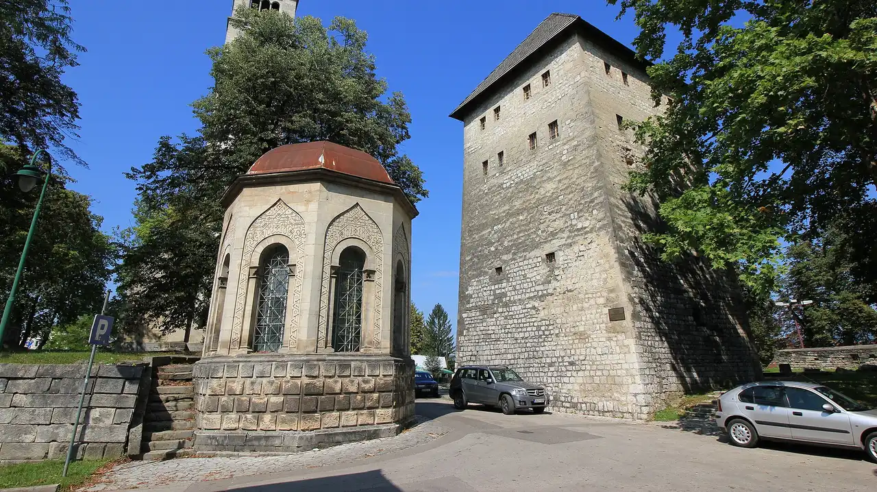 The stone Turbe mausoleum and the medieval Captains Tower side by side in central Bihac under a blue sky