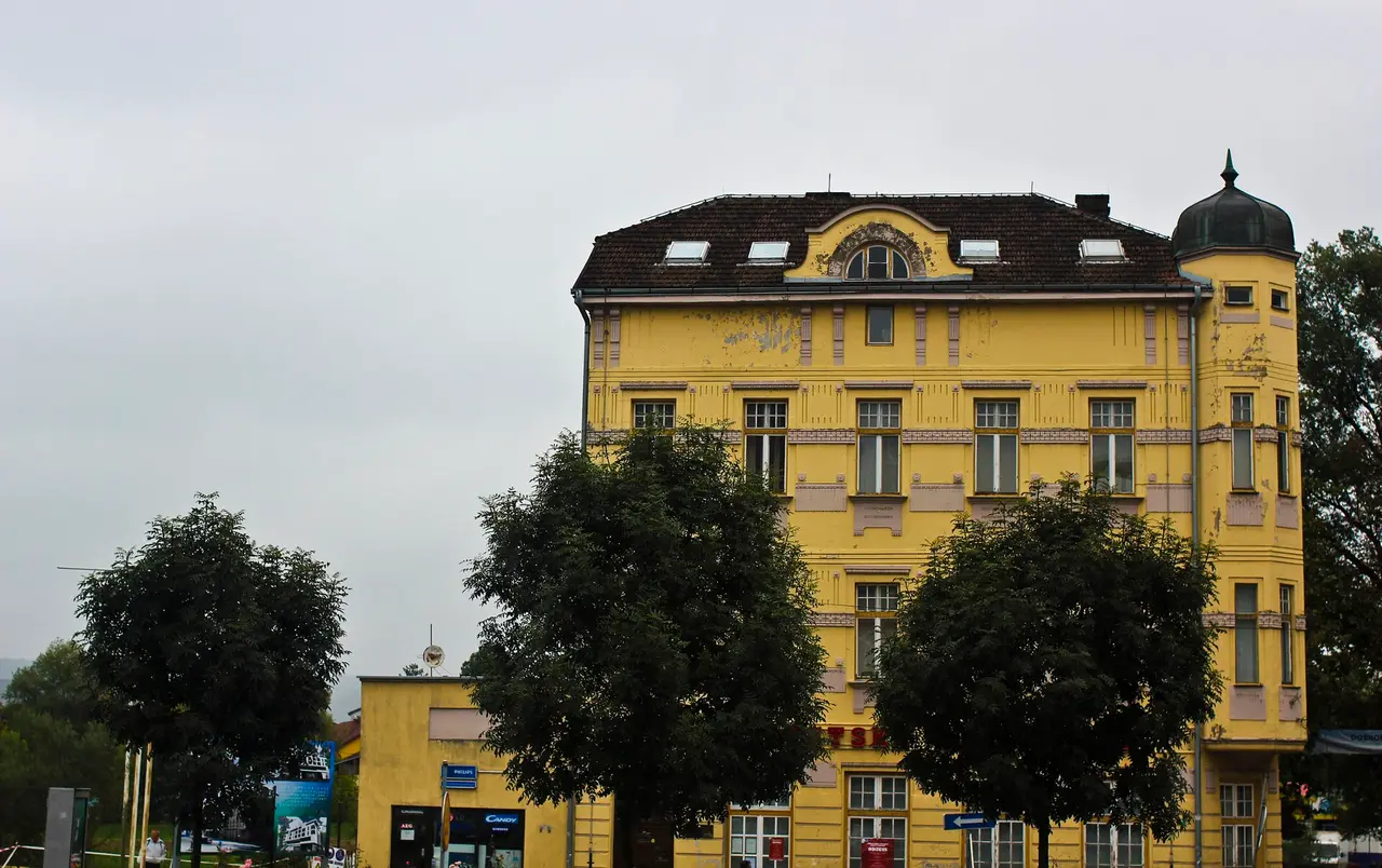 A large yellow Austro-Hungarian apartment block in Bihac with a corner turret and ornamental plasterwork, trees along the pavement in front