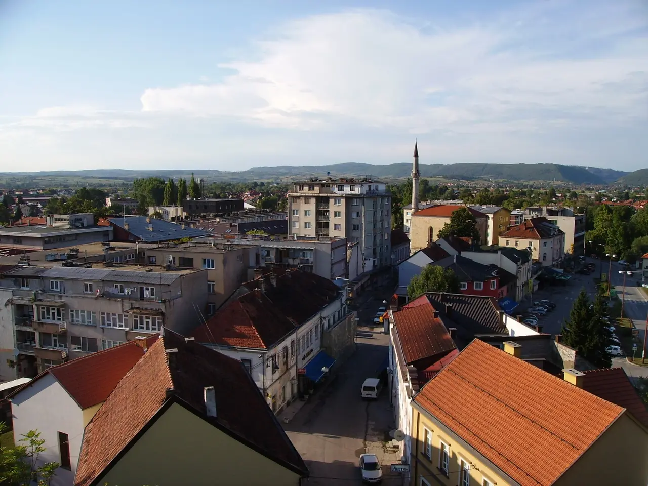 Rooftops of central Bihac seen from the Captains Tower, with the slim minaret of the Fethija mosque rising among red-tiled roofs and green hills behind