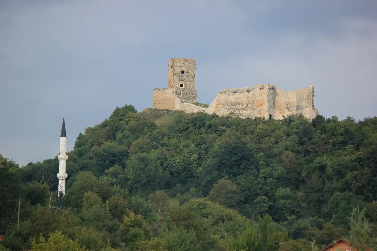 The ruined Sokolac fortress with its square keep on a wooded hilltop near Bihac, a white minaret below in the trees