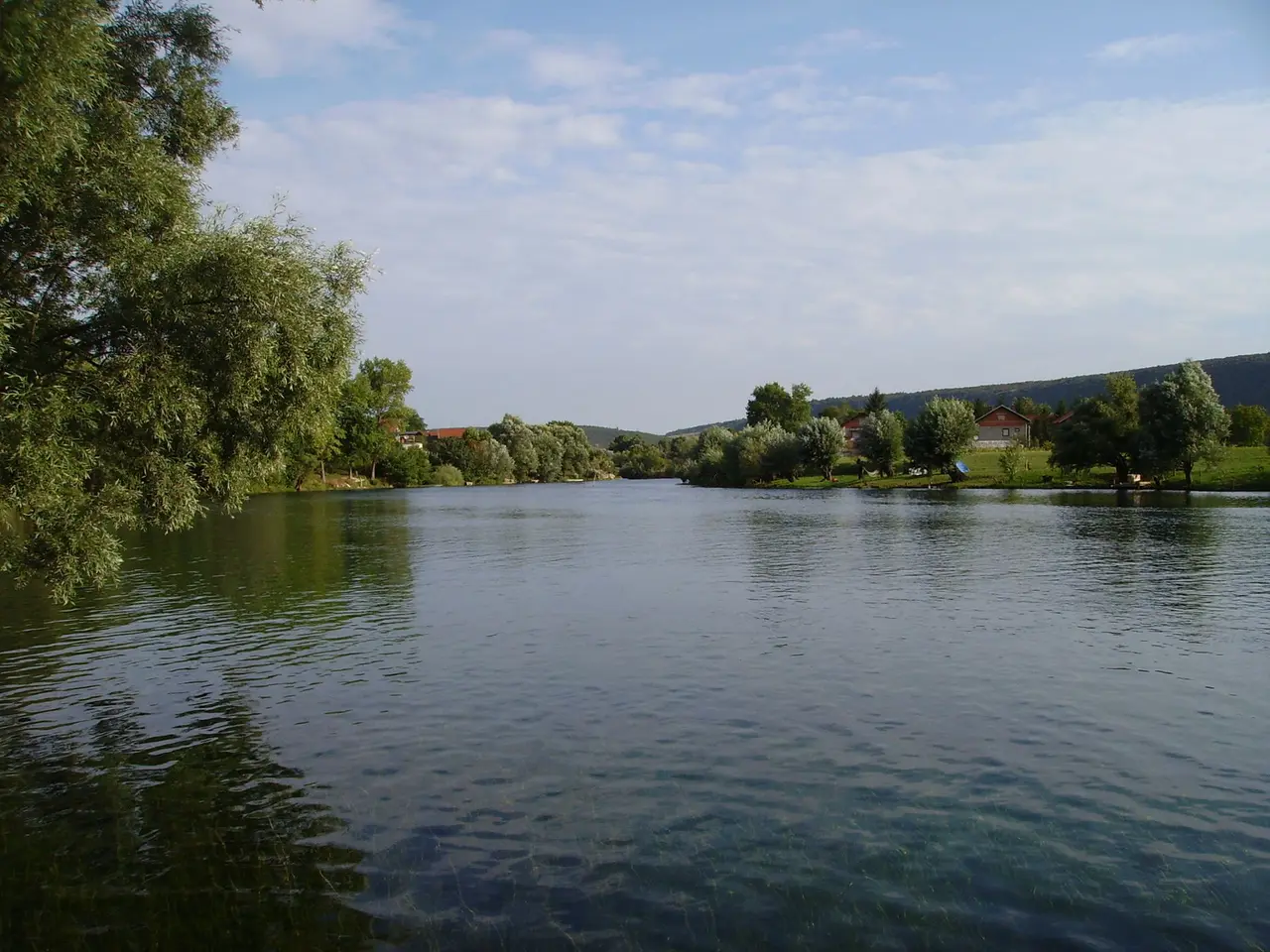 The clear green Una river running past willows and low wooded hills just outside Bihac