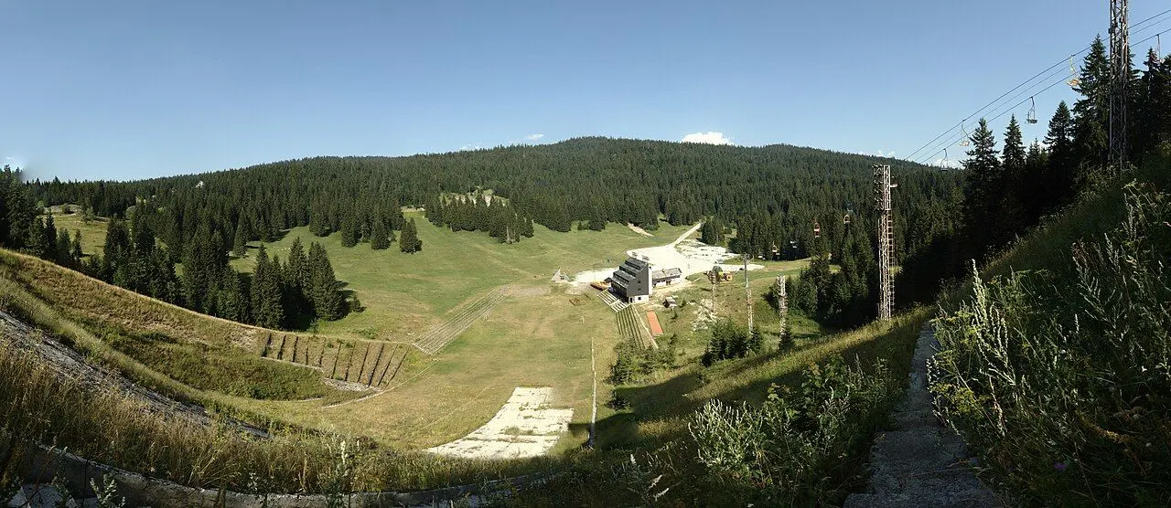 Summer panorama of Malo Polje on Igman, green meadow, forest and chairlift towers below the wooded ridge