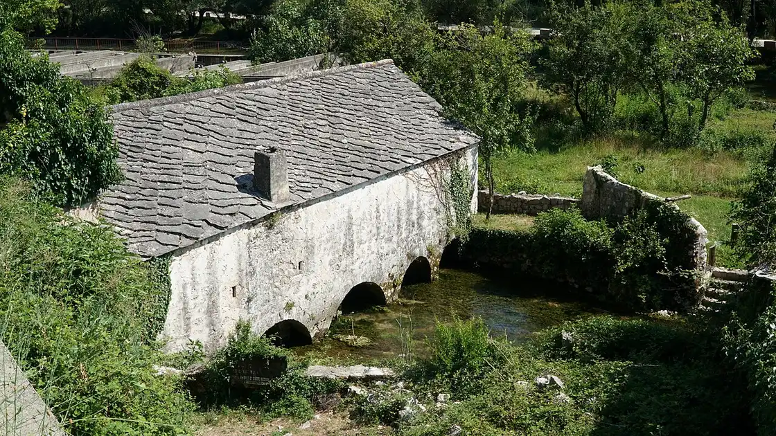 An old wooden water mill standing over the clear Buna river among the trees at Blagaj
