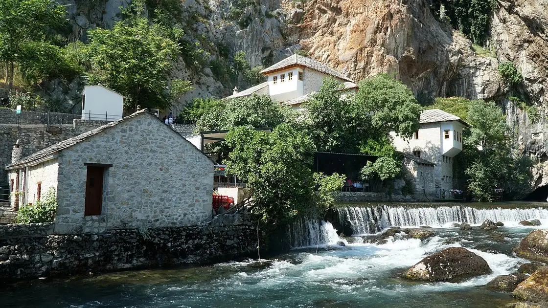 The white Blagaj dervish house at the foot of a tall limestone cliff beside the clear turquoise Buna river