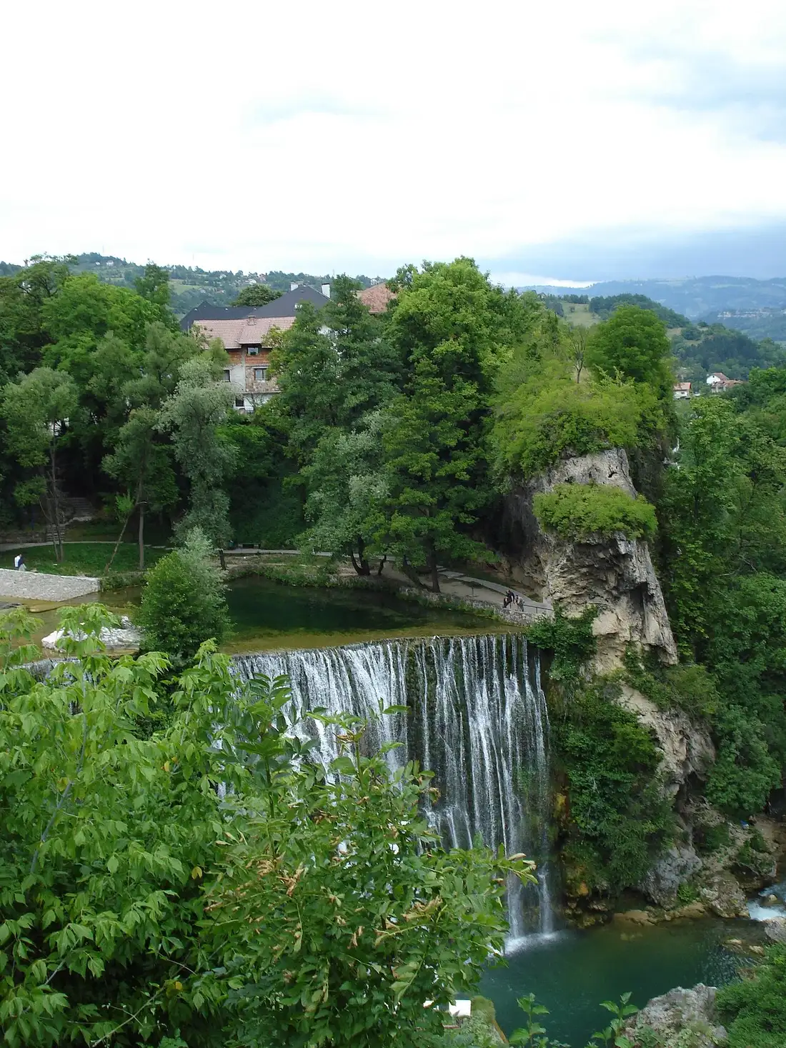 The Pliva Waterfall pouring over a wide ledge in the centre of Jajce, the old town on the hill behind