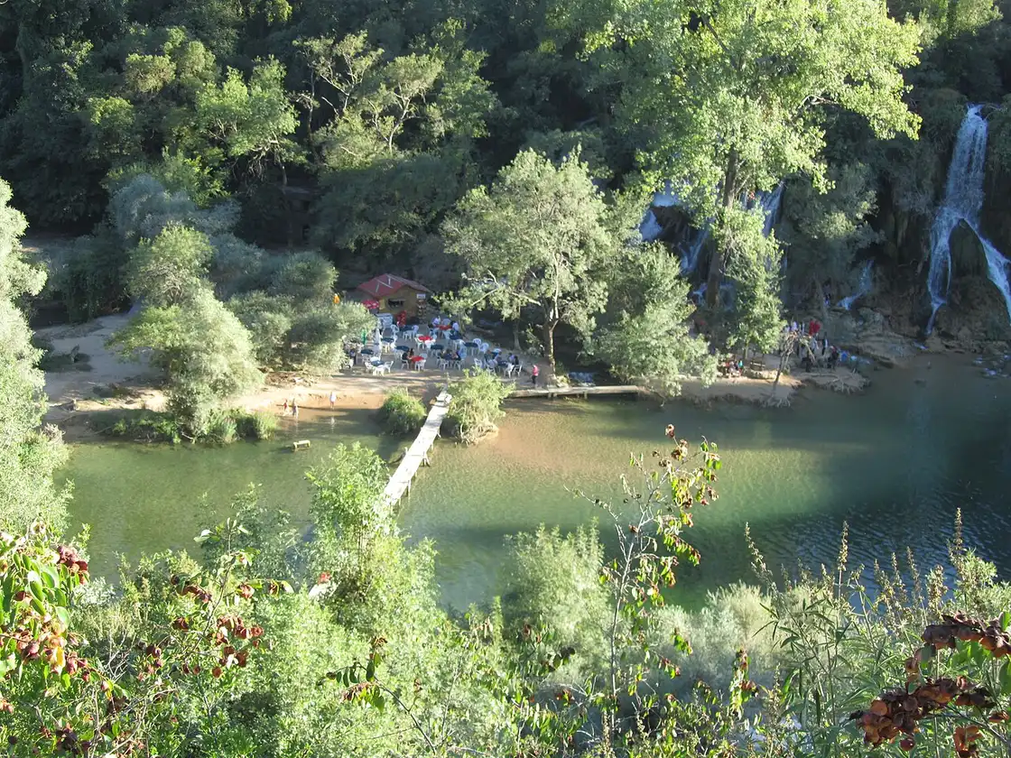 The wide horseshoe of Kravice Waterfalls dropping over a green travertine ledge into a turquoise pool