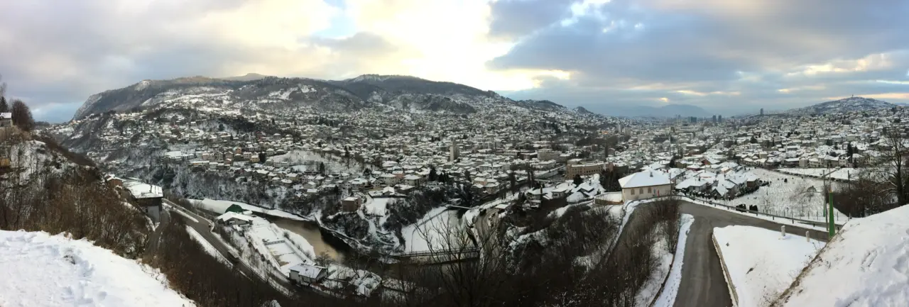 Wide panorama of Sarajevo filling its long valley, minarets and apartment blocks under the surrounding hills