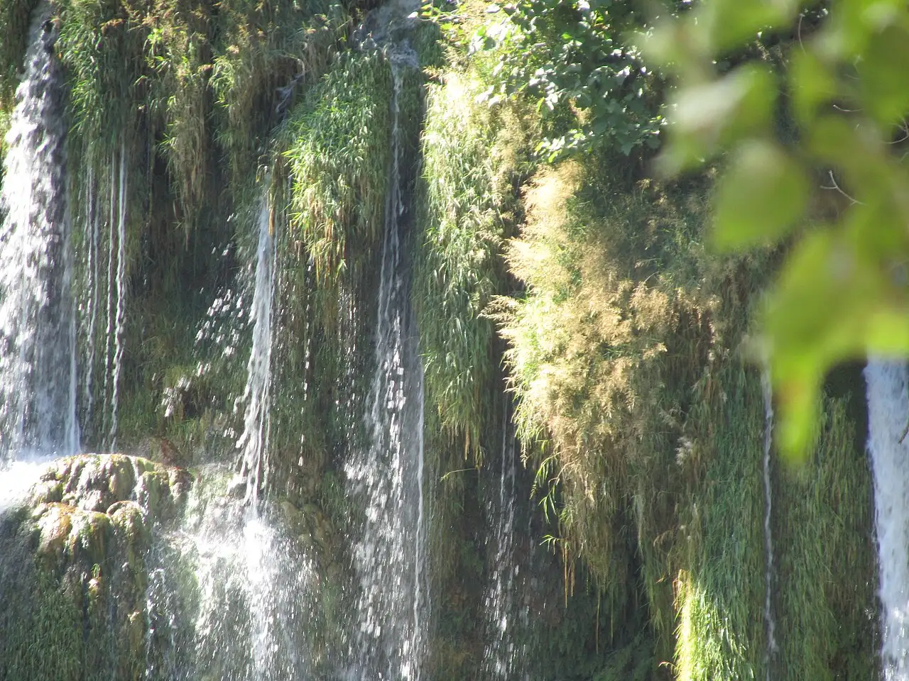 The wide horseshoe of Kravice Waterfalls pouring over a green travertine ledge into a turquoise pool