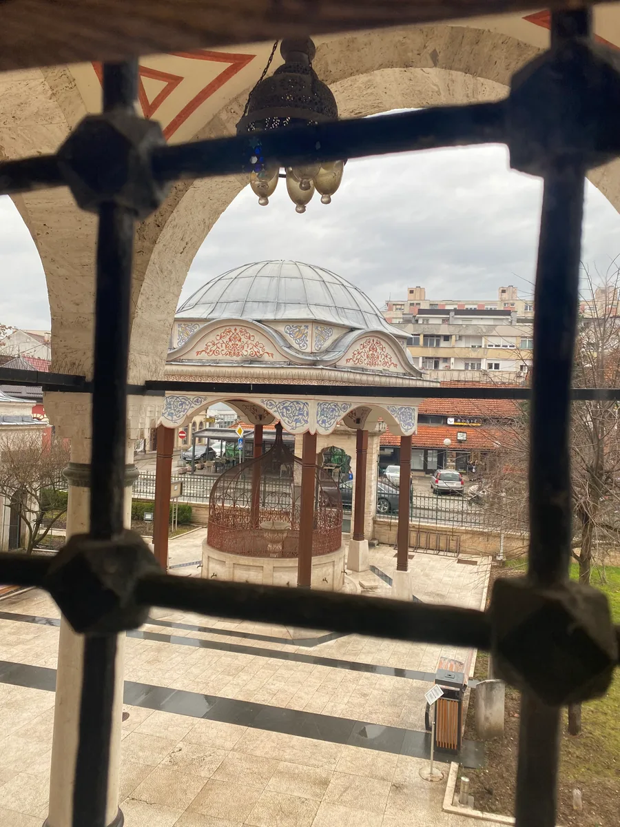 The rebuilt Ferhat Pasha Mosque (Ferhadija) and its fountain in Banja Luka seen through an arched stone porch