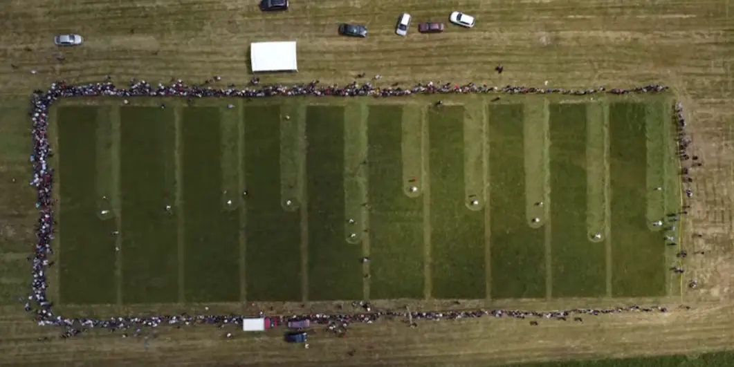 Aerial view of the Strljanica meadow at Kupres, a rectangle of grass divided into mowing lanes and ringed by a dense crowd of spectators