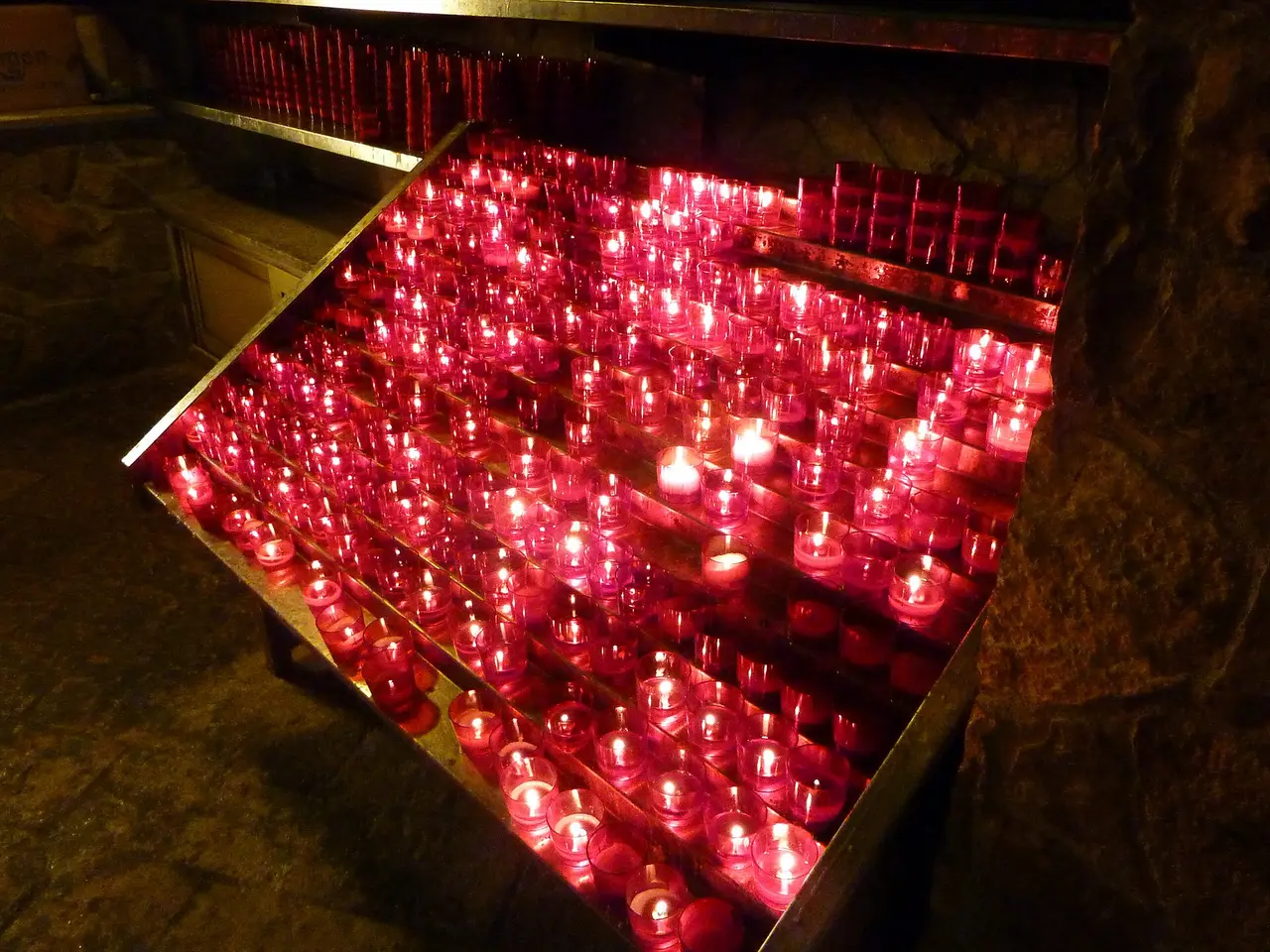 A metal stand in Medjugorje packed with hundreds of burning red votive candles in the dark
