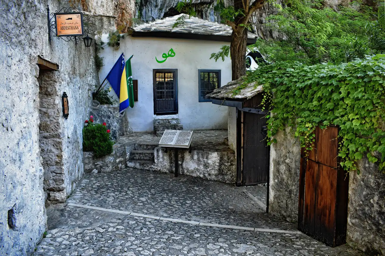 The whitewashed courtyard and prayer house of the Blagaj Tekke dervish lodge, with Bosnian and local flags by the door