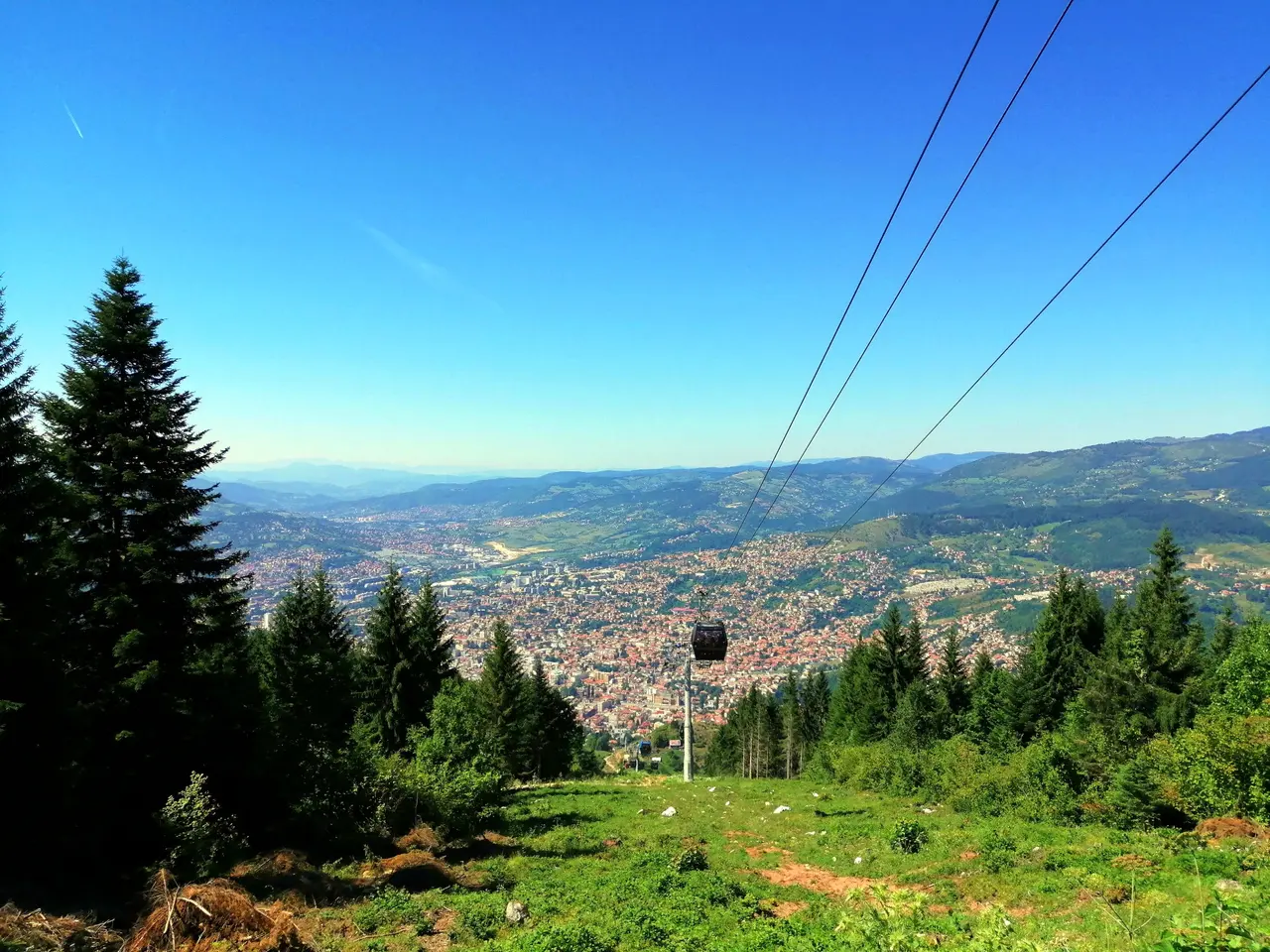 The Trebevic cable car descending over green forest into the Sarajevo valley, the city spread out below