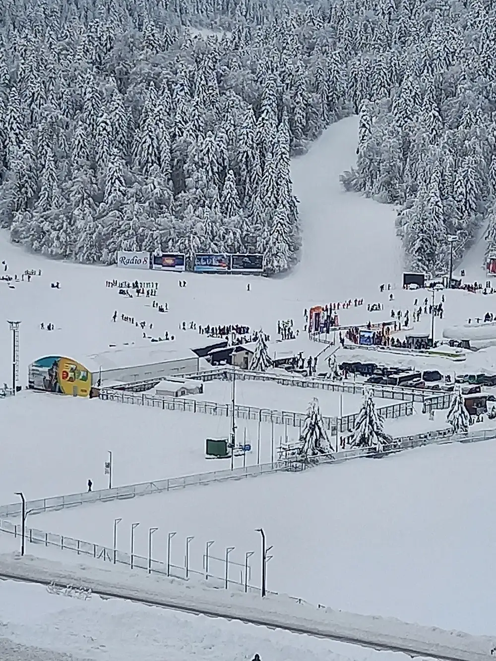 Crowds of skiers at the snowy Babin Do base of Bjelasnica ski resort, surrounded by snow-laden pine forest