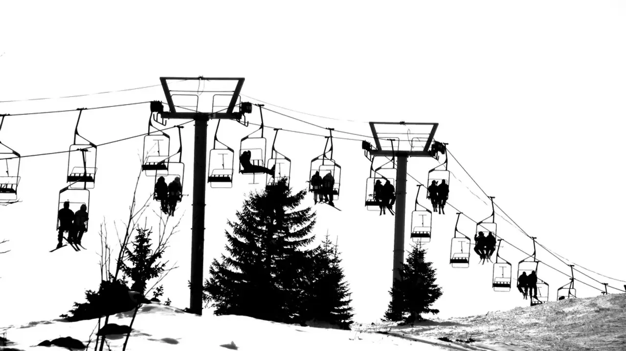 Skiers silhouetted on a chairlift climbing a snowy piste past pine trees at Jahorina ski resort near Sarajevo