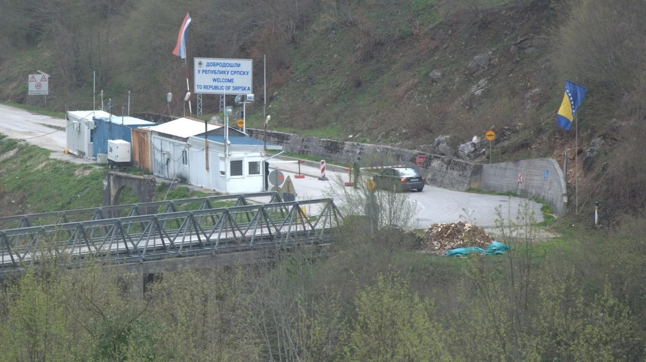 The small Hum border post on the Bosnia and Montenegro frontier, a car pulling away from the barrier past the Welcome to Republika Srpska sign, with the steel road bridge below