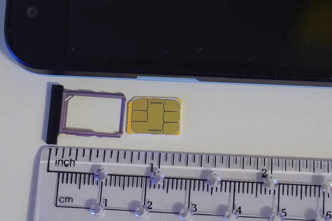 A nano SIM card resting on an ejected phone SIM tray, close up