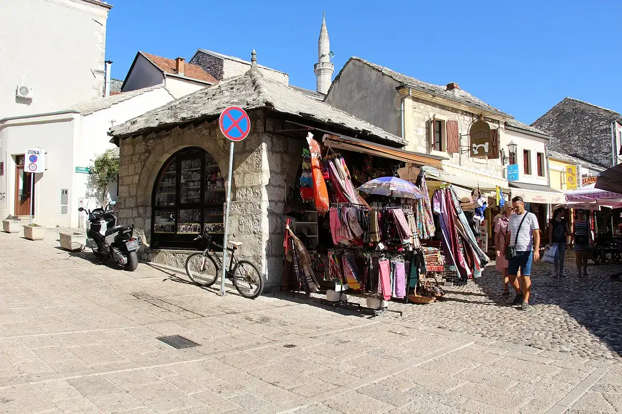 The cobbled bazaar street of Kujundžiluk in Mostar lined with souvenir stalls, a minaret rising behind