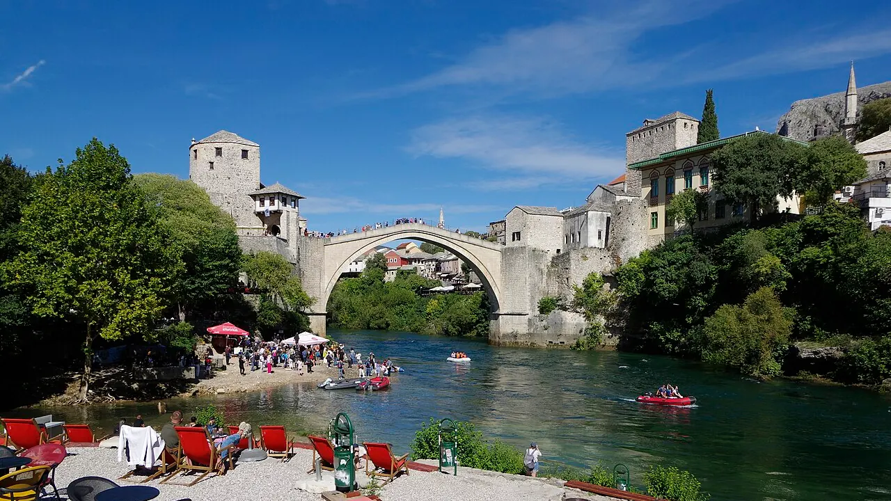 Stari Most arcing over the green Neretva in Mostar with stone houses and hills behind