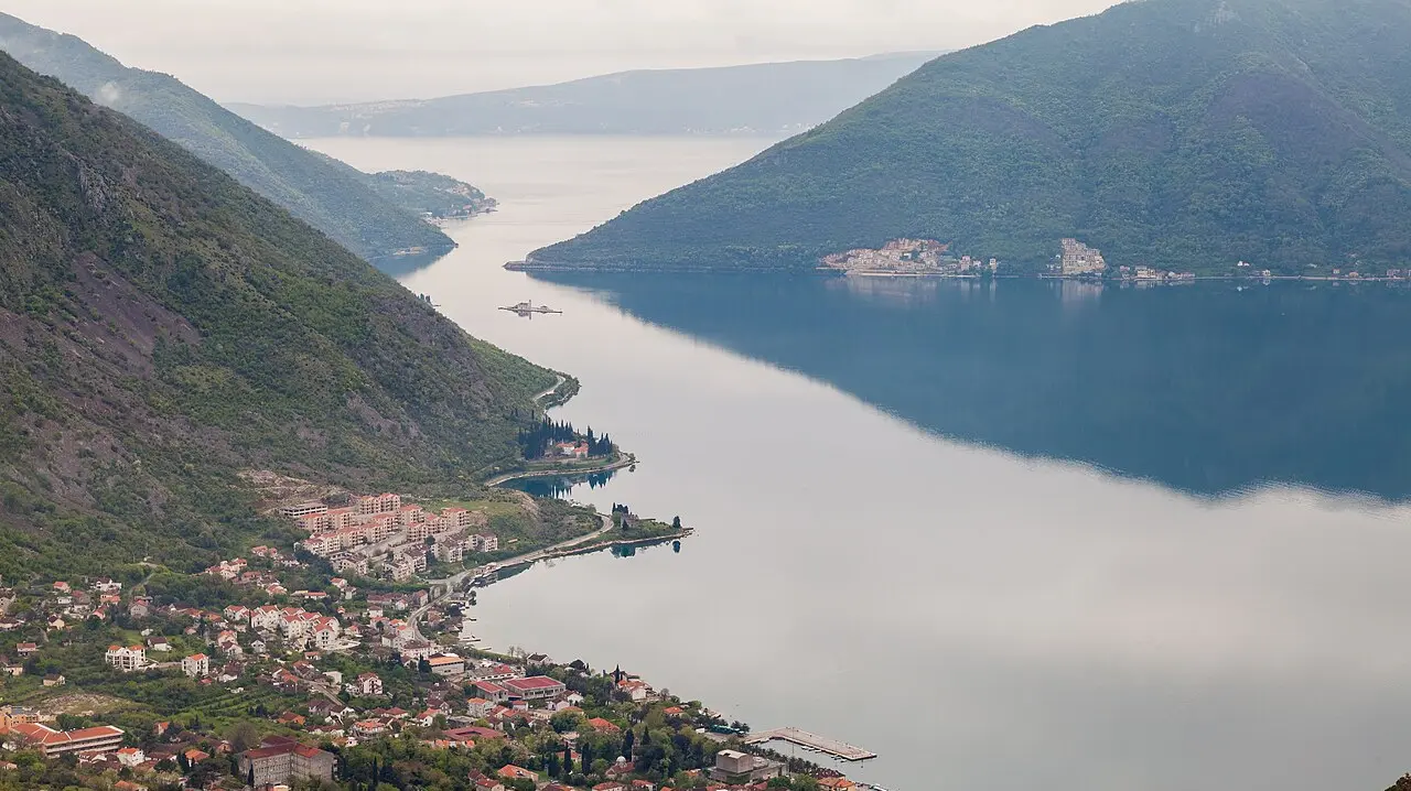 The Bay of Kotor in Montenegro, a still blue inlet ringed by steep grey mountains with a village along the shore