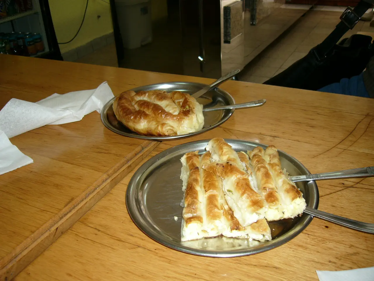 Two metal plates on a buregdzinica table, one with a whole coiled pie and one with a cut pie sliced into fingers