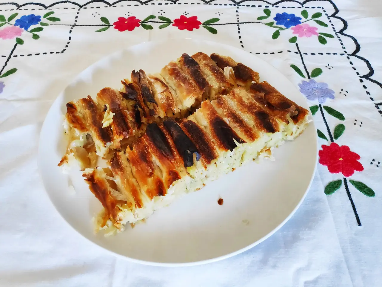 A slab of krompirusa potato pie on a white plate, the coiled pastry scorched dark along the ridges
