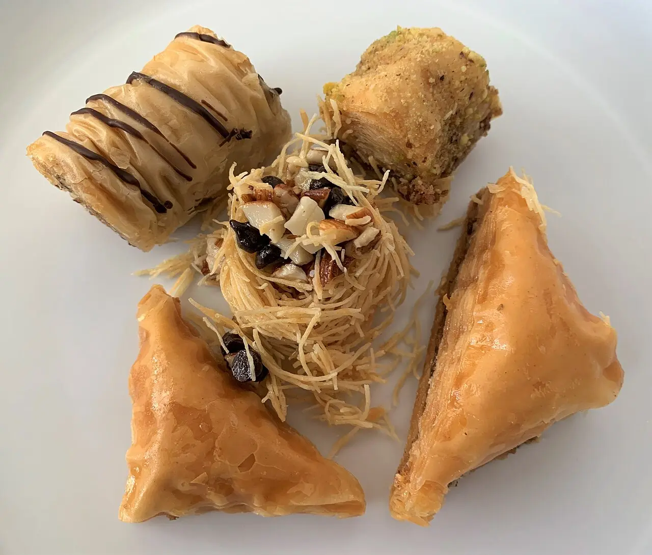 Diamond-cut pieces of walnut baklava soaked in syrup arranged on a white plate