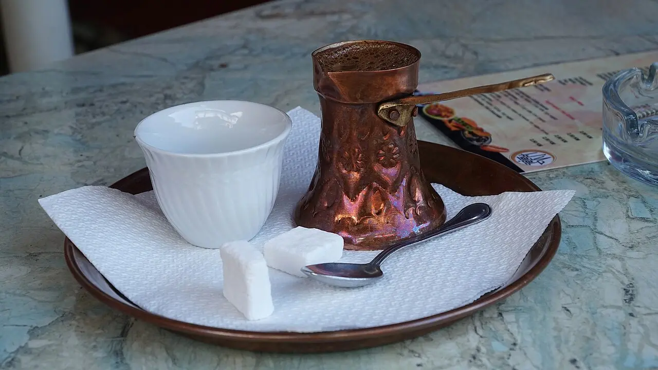 A Bosnian coffee set: a copper dzezva pot, a white handleless fildzan cup, sugar cubes and a spoon on a copper tray in Jajce