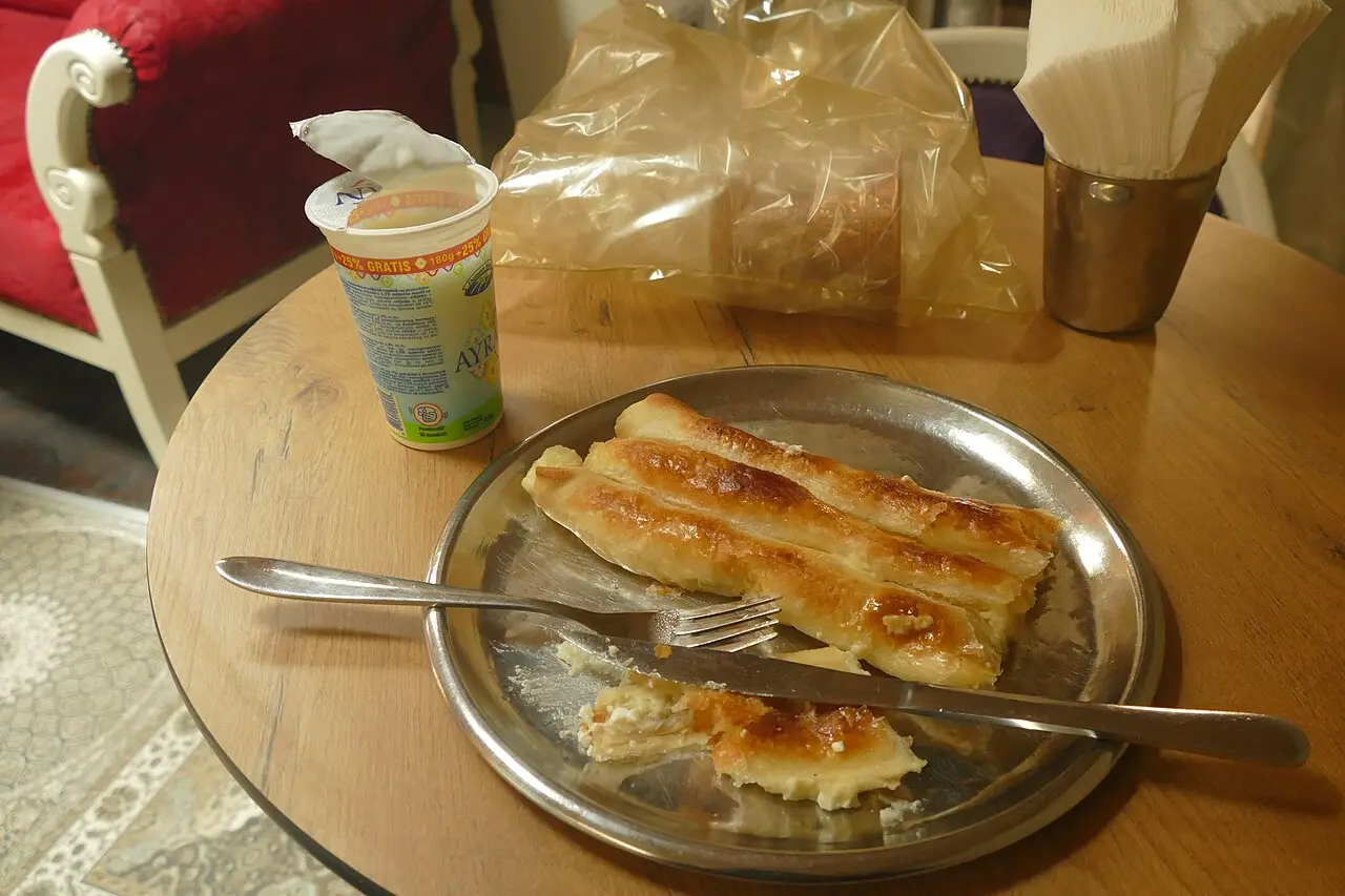 A coiled portion of Bosnian burek pastry on a metal tray, served with a cup of ayran yoghurt drink in Sarajevo