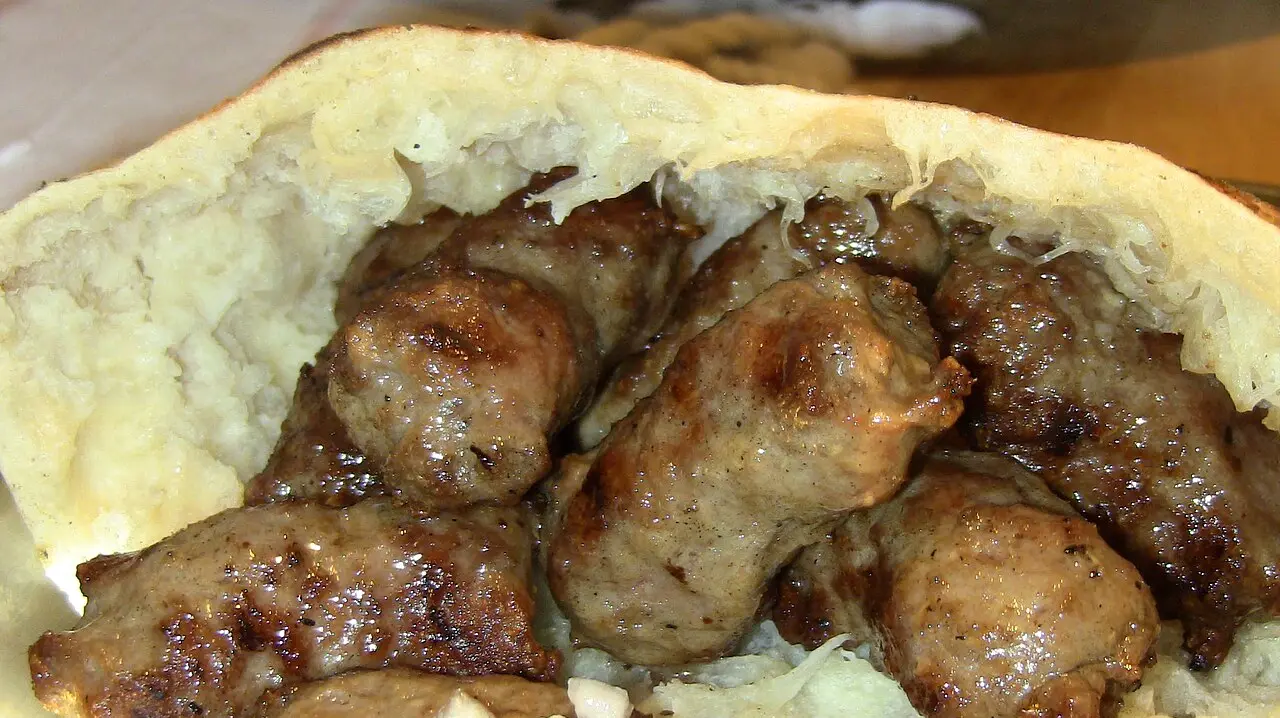 A portion of grilled cevapi minced-meat links tucked into fluffy somun flatbread with chopped raw onion, the national dish of Bosnia