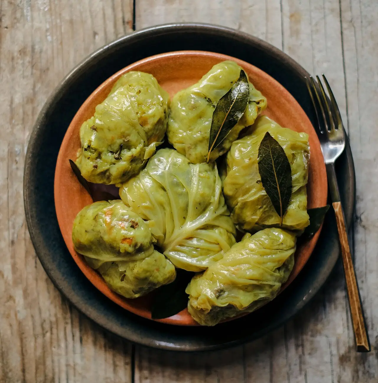 Cabbage-leaf sarma rolls stuffed with minced meat and rice, garnished with bay leaves on an earthenware plate