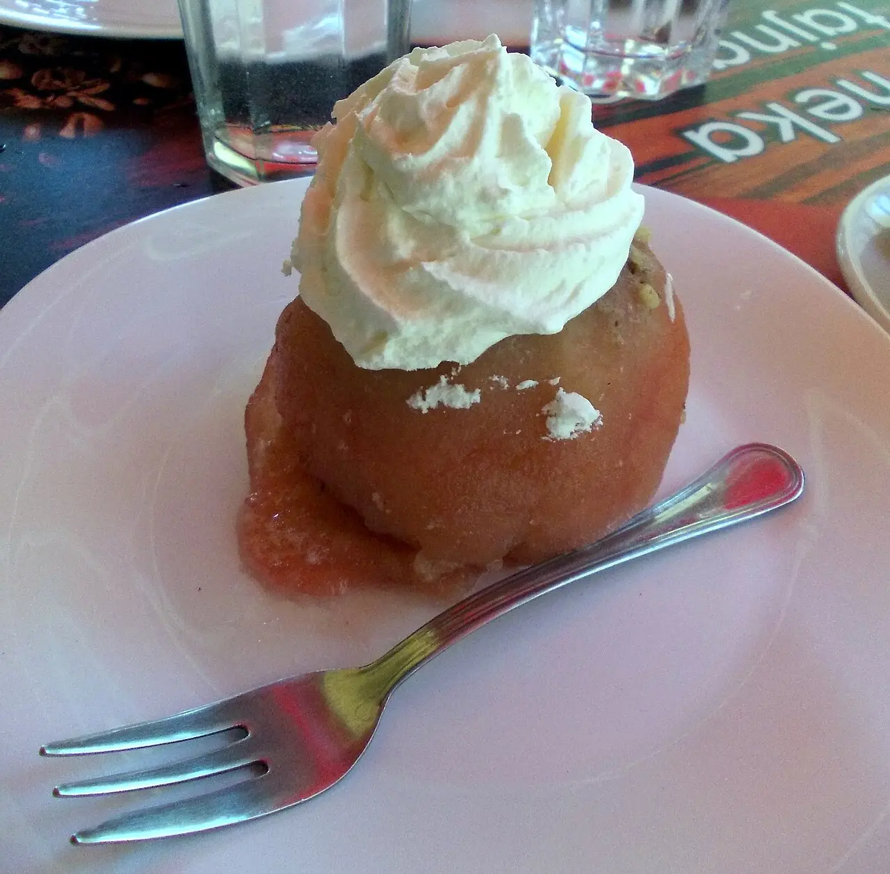 A tufahija dessert: a whole stewed apple stuffed with walnuts and topped with whipped cream on a white plate in Mostar