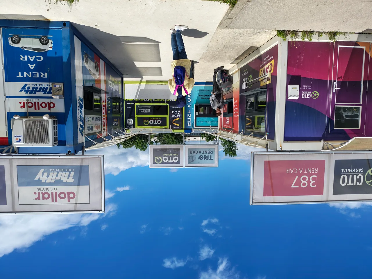 A row of car-rental kiosks at Sarajevo airport with company signs and travellers walking between them