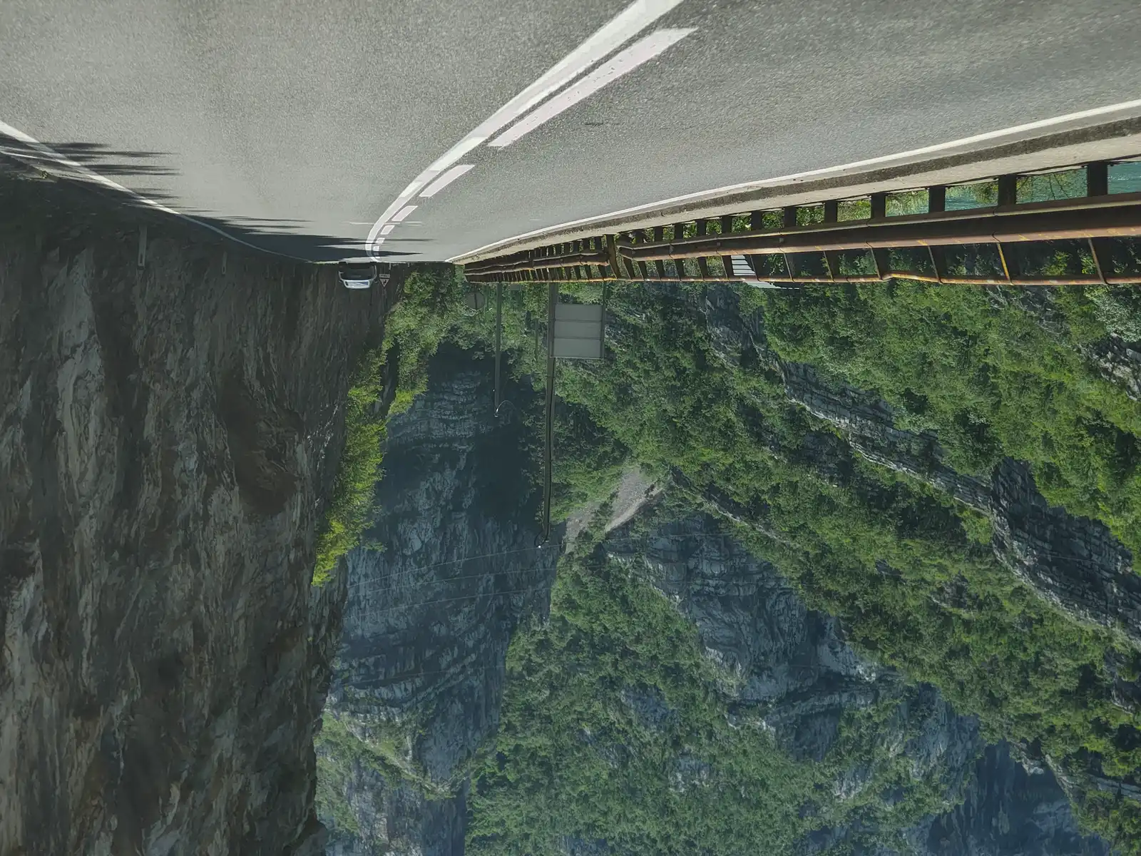 A two-lane road hugging a limestone cliff through the green Neretva canyon in Herzegovina, a car ahead and the river guardrail on the left