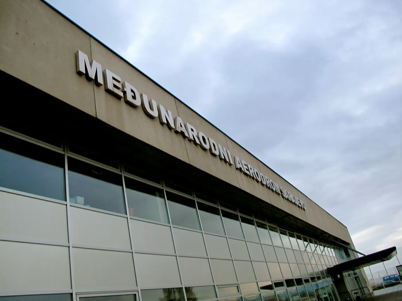 The angled facade of Sarajevo International Airport with its Medunarodni Aerodrom Sarajevo sign under a cloudy sky