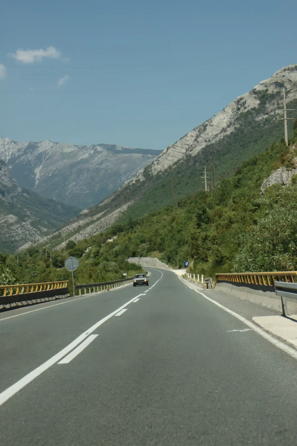 A two-lane road curving through the green Neretva valley toward Mostar, mountains rising on both sides