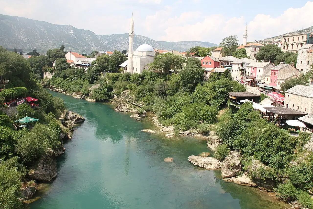 The turquoise Neretva river winding through Mostar between stone houses, minarets and mountains