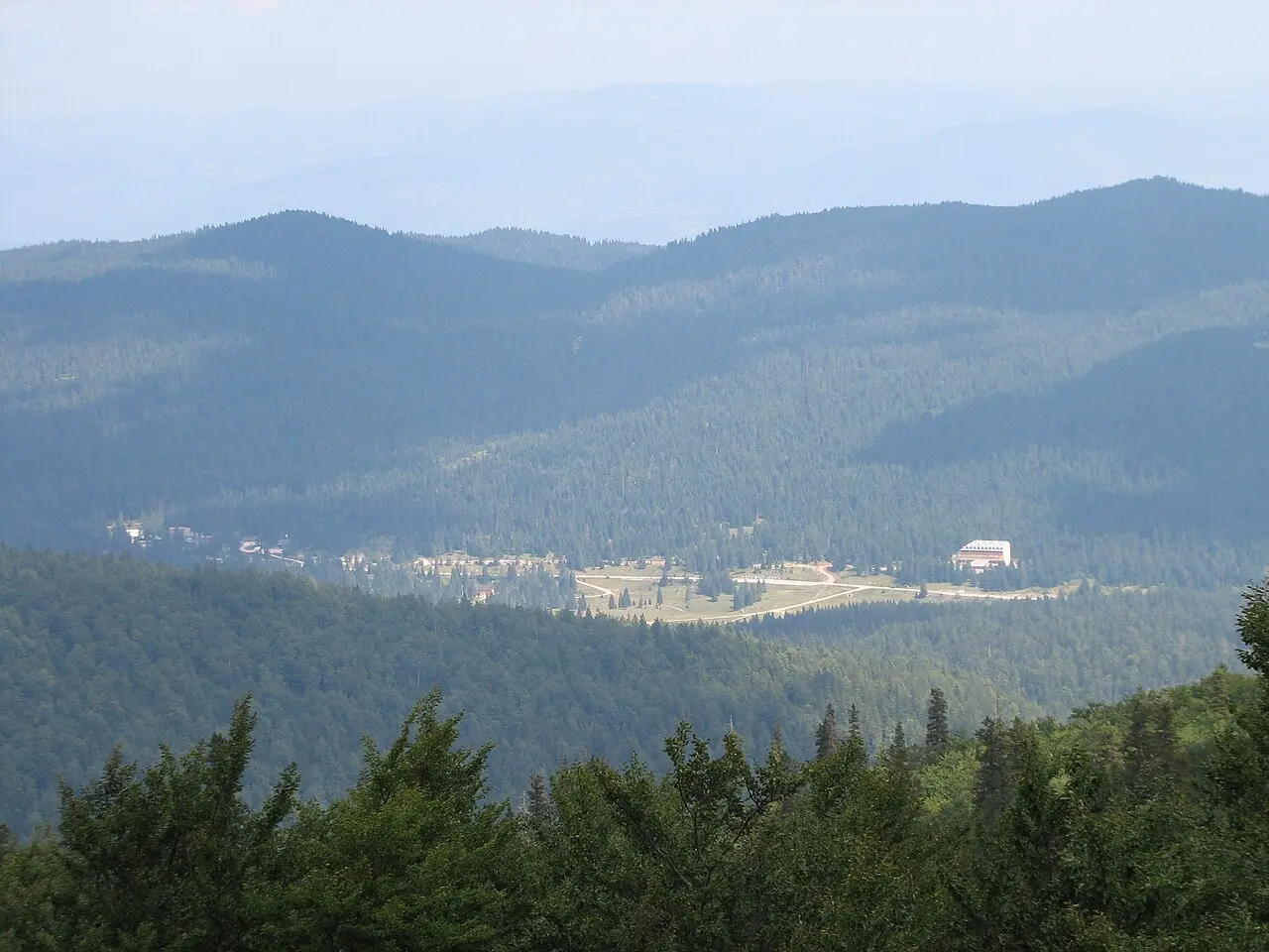 The green Olympic ski slopes above Sarajevo in summer, empty and rolling towards distant peaks