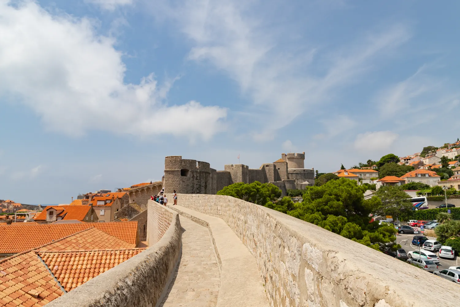Visitors walking the stone city walls of Dubrovnik Old Town, red-tiled roofs and the Minceta fortress ahead