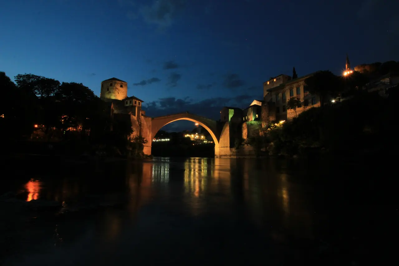 The Old Bridge in Mostar lit up at night, reflected in the dark Neretva river
