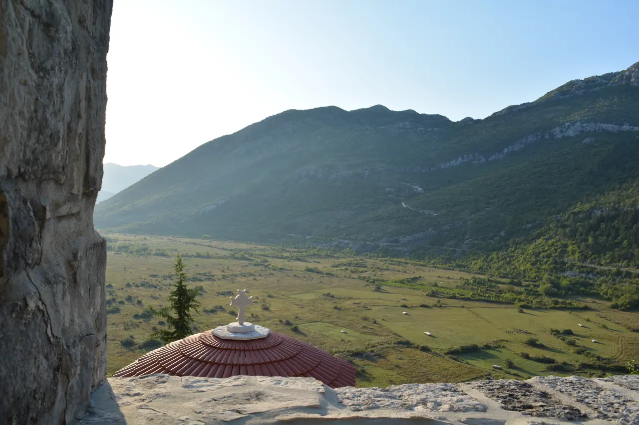 The rooftop cross of Zavala monastery overlooking the green karst valley of Popovo polje at sunset