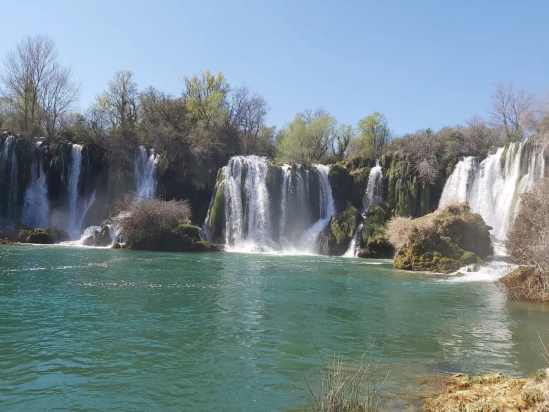 The wide curtain of Kravice waterfalls tumbling into a green swimming pool in Herzegovina, a common detour on the Dubrovnik to Mostar route